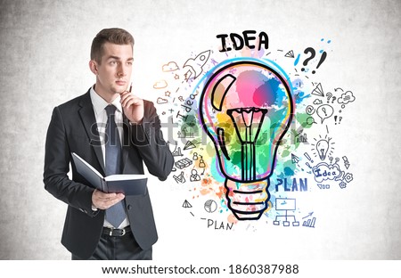Thoughtful young businessman with book standing near concrete wall with colorful business idea sketch drawn on it
