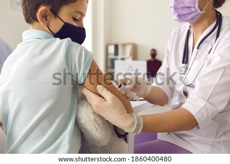 Immunisation. Protecting children from diseases. Close-up nurse in medical gloves giving injection to little patient. Brave boy in face mask getting a flu shot at doctor's office and looking at needle Royalty-Free Stock Photo #1860400480