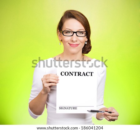 Closeup portrait smiling, young business woman with glasses holding contract pointing with pen at space for signature isolated green background. Positive face expression emotion, attitude, perception