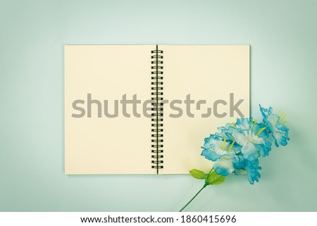 Top Table Spiral Notebook or Spring Notebook Mockup in Unlined Type on Center Frame and Blue Flowers at Bottom Right Corner on Blue Pastel Minimalist Background in Vintage Tone