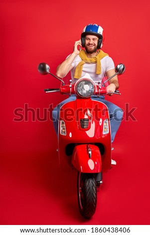 positive male talk on phone while driving a motorbike, handsome guy in casual wear sits enjoying driving, isolated on red background