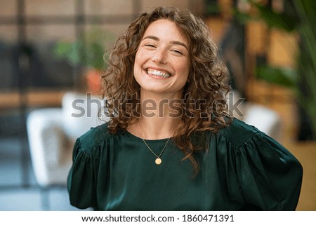 Portrait of beautiful young woman laughing at creative office. Happy businesswoman with curly hair excited with toothy smile. Enthusiastic cheerful girl looking at camera. Royalty-Free Stock Photo #1860471391