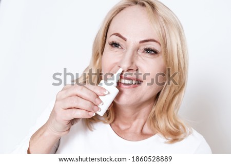 Woman buries her nose with a nasal spray and smiles. The blonde stands on a white background and bury her nose with the drug.  Royalty-Free Stock Photo #1860528889