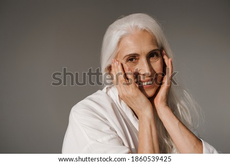 Happy elderly white-haired woman smiling and looking at camera isolated over grey background