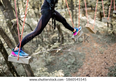 Young well-equipped woman having an active recreation, climbing ropes in the park with obstacles outdoors, close-up on legs