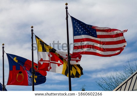 Three flags are waving on separate flags poles against blue sky on a windy and partly cloudy day. From right to left they stand for: USA, state of Maryland and Montgomery County