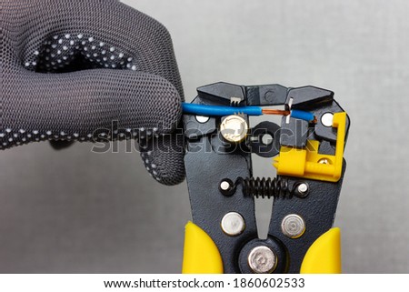 An electrician wearing gray work gloves is stripping electrical wires with a stripper. Royalty-Free Stock Photo #1860602533
