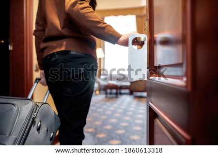 Cropped shot of middle-aged businessman in casual wear with suitcase entering his room. A door with a sign. Horizontal shot. Selective focus