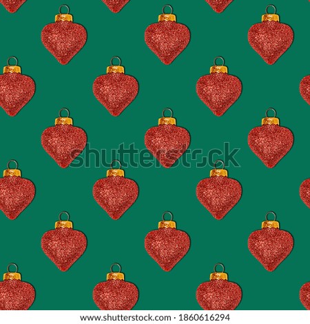 Seamless Christmas pattern with decorative shiny toys in the shape of a heart on a green background. Xmas abstract backdrop. Top view