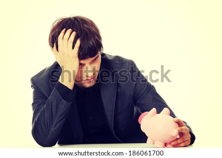 Young depressed businessman holding piggy bank. Economy crisis concept 