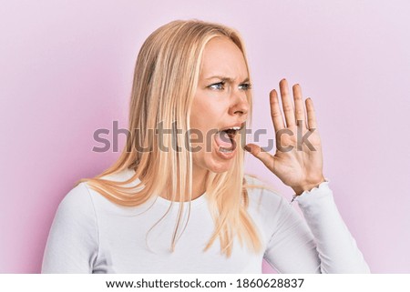 Young blonde girl wearing casual clothes shouting and screaming loud to side with hand on mouth. communication concept. 
