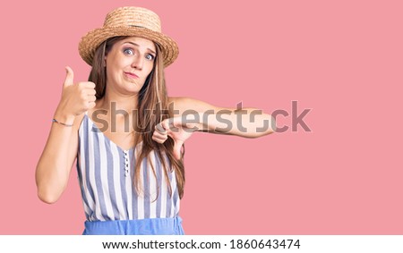 Young beautiful blonde woman wearing summer hat doing thumbs up and down, disagreement and agreement expression. crazy conflict 
