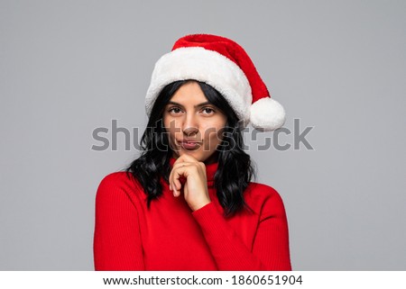 Portrait of a cute christmas woman with a red santa claus hat, finger on chin, confused, thinking what to shop for the holiday season.