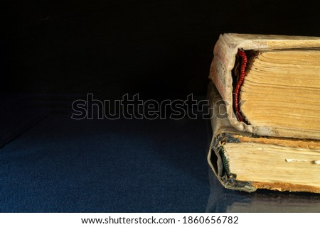 Aging book rests upon glass table with reflection. Subjects on black background close-up