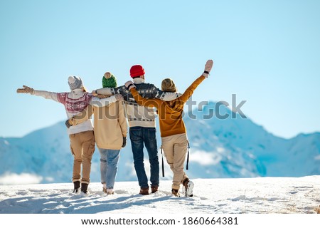 Four happy friends are standing and embracing against snow capped mountains at sunny day. Winter vacations concept Royalty-Free Stock Photo #1860664381