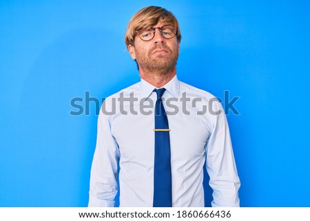 Young blond man wearing business clothes and glasses relaxed with serious expression on face. simple and natural looking at the camera. 