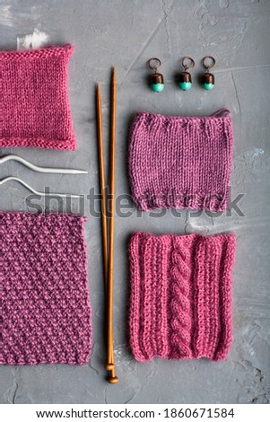 Top view: knitting accessories and samples of knitted products lie on a gray concrete background. Place for inscription.