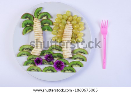 Fruit dessert. Picture tropical trees made of bananas, kiwi, tangerines, grapes on a plate.