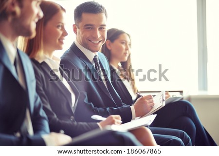 Row of business people making notes at seminar with focus on smiling young man Royalty-Free Stock Photo #186067865