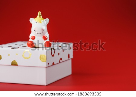 Unicorn figurine on a gift box on a red background with free space.