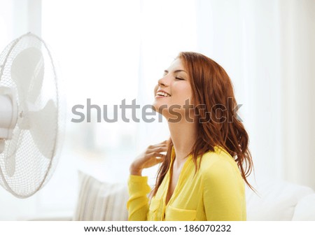 summer, weather and equipemt concept - smiling redhead teenage girl with big fan at home Royalty-Free Stock Photo #186070232