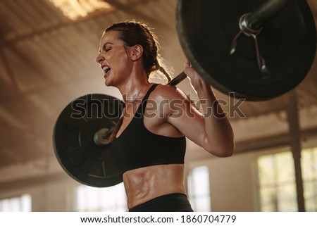 Female bodybuilder doing exercise with heavy weight bar. Fitness woman sweating from squats workout at gym. Female putting effort and screaming while exercising with heavy weights. Royalty-Free Stock Photo #1860704779