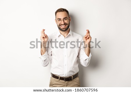 Hopeful optimistic man making a wish, cross fingers and praying, standing over white background