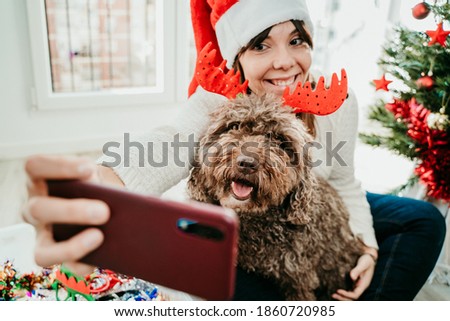 Young funny woman dressed up with Christmas props playing with her cute dog at home. Taking pictures together at christmas time. Lifestyle
