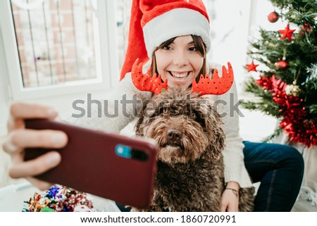 Young funny woman dressed up with Christmas props playing with her cute dog at home. Taking pictures together at christmas time. Lifestyle