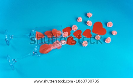 Two champagne glasses with bright hearts and small roses on a blue background. The concept of celebrating Valentine's Day. Romantic atmosphere of the holiday. copy space. Flat lay. top view