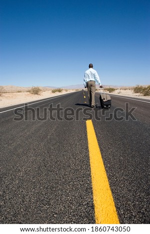 Rearview of a businessman with luggage in the middle of the deserted highway.