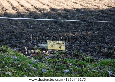 Electric fence for cattle to protect the garden production from wild animals. Yellow Sign that says ¨ electric fencing ¨ in spanish and has a drawing to be careful not to touch it