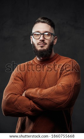 Posing in dark background with crossed arms strong guy in sweater with glasses and beard.
