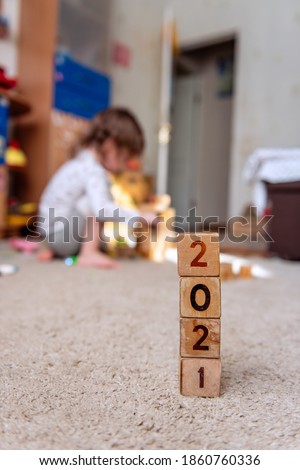 Wooden cubes with 2021 numbers are in a row. A small Child is building a tower against a blurred background. Home active games. Construction, real estate of the future home. Happy family. Copy space