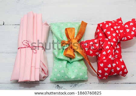 Wrapping gift for Valentine's Day, Birthday, Mother's Day using pink, green, red cotton textile on  wooden background. Furoshiki, ecological gift wrapping