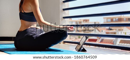 Horizontal view girl sit cross-legged on mat do meditation practice at home in terrace sunny warm day view. Use tablet listen calm music in state in deep relaxation, app user modern tech, yoga concept