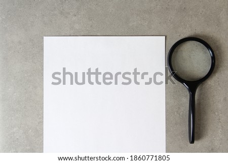 Template of white paper with a magnifying glass on light grey concrete background. Concept of new idea, business plan and strategy, development and implementation of content. Stock photo with empty