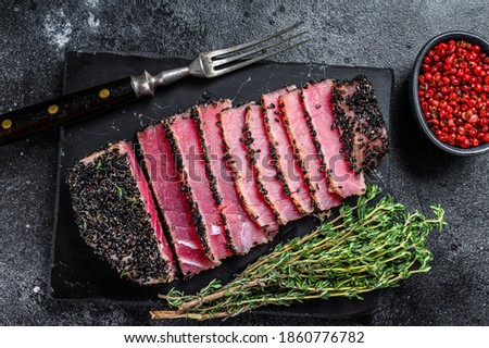 Rare Ahi tuna steak slices with fresh herbs on a cutting board. Black background. Top view Royalty-Free Stock Photo #1860776782