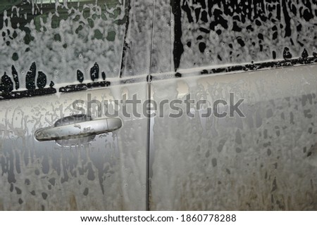 The car body is covered with soap suds to remove dirt. Car wash