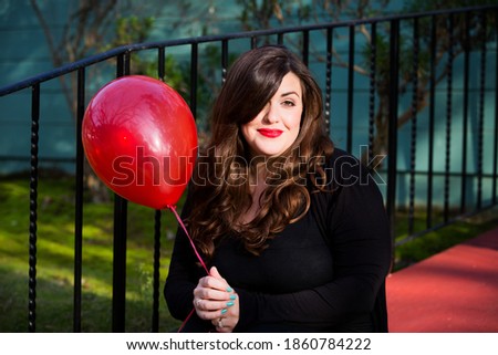 portrait of beautiful brunette woman sitting outside holding a red balloon