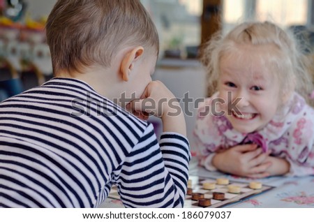 Cute little girl grinning mischievously at her brother as they sit at a table together playing a game of checkers or draughts