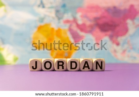 The word Jordan written with wooden dices in front of a purple background and a geographic map