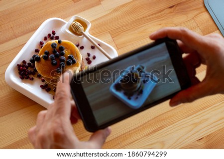woman taking a photo of pancakes decorated with tropical pomegranate banana kiwi berry on a white plate on a wooden table