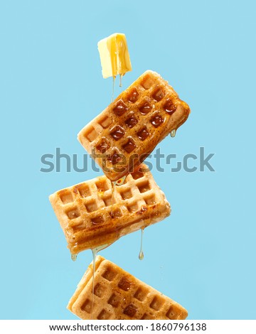 Flying waffles and butter getting dripped with maple syrupo over a light blue background Royalty-Free Stock Photo #1860796138