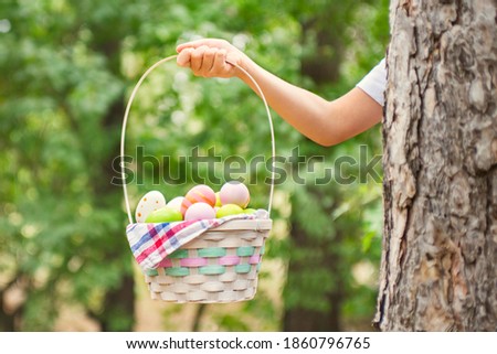 Child hand holding basket full of colorful easter eggs after egg hunt at spring time. Happy Easter day.