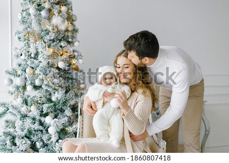 Happy family celebrates Christmas and New Year at home in the living room near the Christmas tree. Family portrait of dad, mom and baby Royalty-Free Stock Photo #1860807418