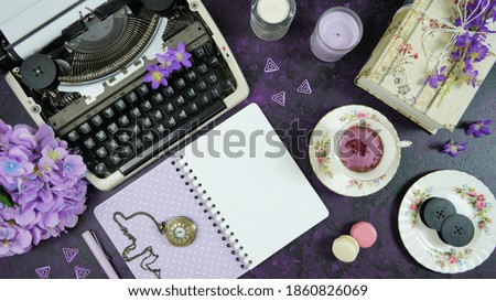 Purple theme vintage writers desktop workspace with typewriter, lavendar tea, hibiscus flowers and old books on stylish purple textured background. Top view blog hero header creative flat lay.