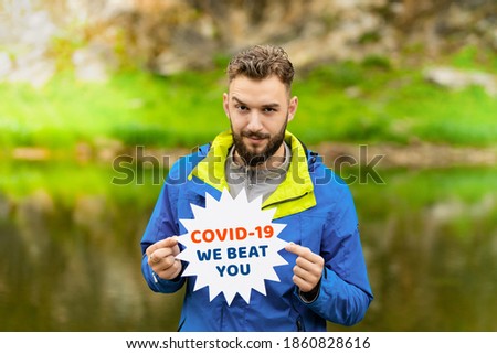 A young man in a blue jacket stands in the countryside in summer and holds the message of the virus we beat you. Medicine and health care. Pandemic Concept 2020. nature