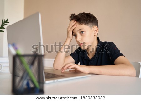Smart looking boy doing his homework and look at computer notebook at home due to Covid-19 pandemic and social distancing, New normal, Remote class. High quality photo