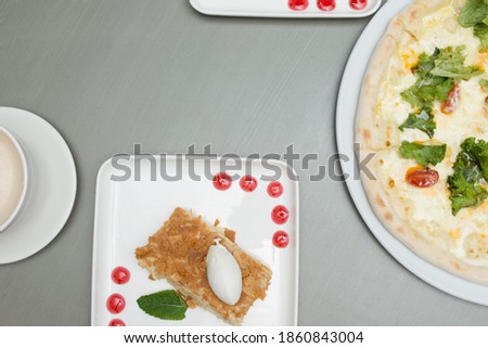Slice of Napoleon cake, cocoa and pizza on a gray background. Slice of ice cream on the cake, pizza with herbs and cappuccino on the table. Cake with ice cream, moccasin and vegetarian pizza on table.